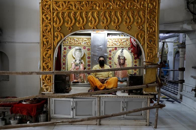 A priest wearing a protective mask sits behind a wooden barrier installed to maintain social distancing inside a temple after the opening of most of the religious places after India eases lockdown restrictions that were imposed to slow the spread of the coronavirus disease (COVID-19), in New Delhi, India, June 8, 2020. REUTERS/Anushree Fadnavis